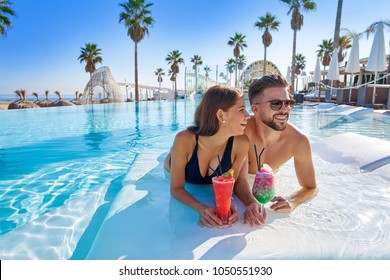 Young tourists couple on infinity pool drinking cocktails at resort on the beach - Powered by Shutterstock