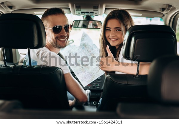 Young tourists smiling couple handsome\
man and beautiful woman travelling on vacation by car checking the\
map looking happy lady showing like honey moon\
trip.