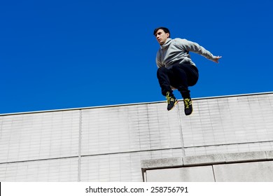 Young tracer athlete jumping over building roof against blue sky background, free runner performing in action, young risky man jumping from high rooftop at sunny day - Powered by Shutterstock