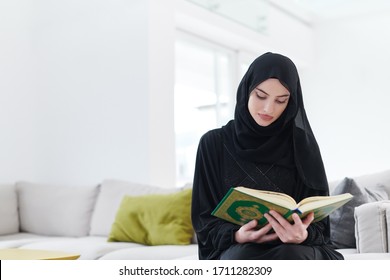 young traditional muslim woman reading Quran on the sofa before iftar dinner during a ramadan feast at home - Powered by Shutterstock