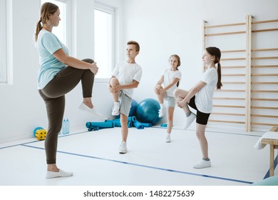 Young Trainer And Group Of Kids Warming Up Before Sport Classes