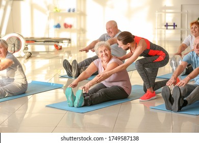 Young Trainer Helping Elderly People During Training In Gym