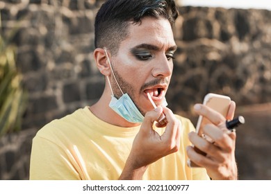 Young Transgender Man With Make Up Apply Lipgloss With Mirror While Wearing Safety Face Mask Under Chin