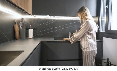 Young transgender woman in sleepwear placing coffee pot on automatic stove in modern kitchen at home - Powered by Shutterstock