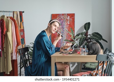 Young Transsexual Sitting At The Table And Applying Makeup On His Face In Dressing Room