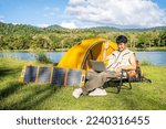 Young travel man relax and enjoy talking calling on video on laptop, using laptop computer work remotely anywhere using internet connected to portable solar panel charging