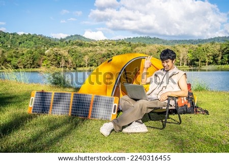 Young travel man relax and enjoy talking calling on video on laptop, using laptop computer work remotely anywhere using internet connected to portable solar panel charging