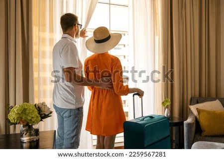 young traveler couple with luggage looking out of the hotel room window after arrival