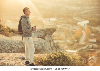 Young traveler drinks a hot drink in the mountains. From the mug of tea comes steam. Athlete on vacation