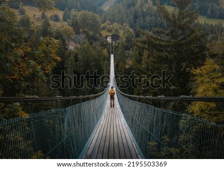 Young traveler man dressed in yellow jacket crosses hiking on an impressive wooden and metal bridge in the village of Goms in the Swiss alps