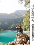 Young traveler is resting and taking pictures of amazing landscape with mountains and lake on smartphone during vacation. Tourism, nature, blogging concept.