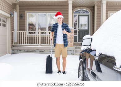 Young Traveler Standing Next To His Car In The Snow With His Suitcase. He Is Wearing A T Shirt, Shorts And A Santa Hat.