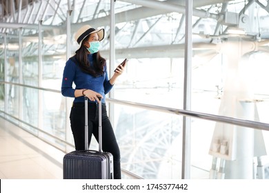 Junge Reisende tragen Maske und stehen im Terminal International Airport mit schwarzem Gepäck. Halten Sie das Smartphone in der Hand und schauen Sie aus der Halle, während Sie die Flugverzögerung hören