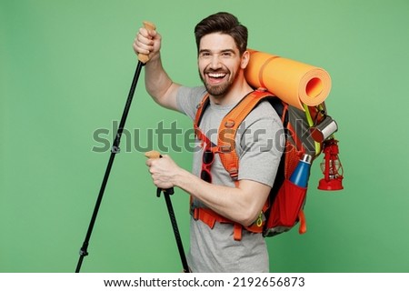 Young traveler white man carry backpack stuff mat hold trakking poles isolated on plain green background. Tourist leads active healthy lifestyle walk on spare time Hiking trek rest travel trip concept