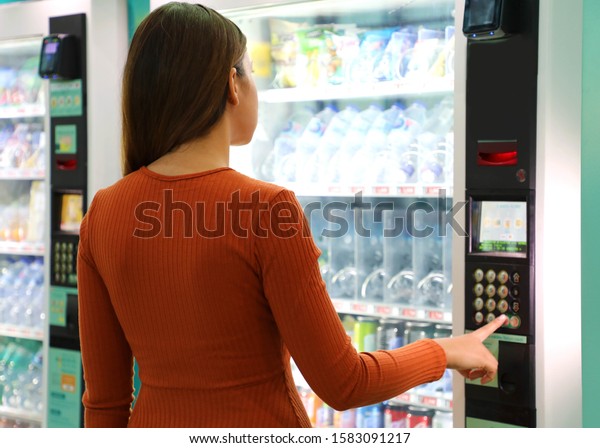 Young traveler woman\
choosing a snack or drink at vending machine in airport. Vending\
machine with girl.