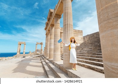 Young Traveler Woman With Greek Flag At The Ancient Greek Ruins. Tourism In Greece Concept