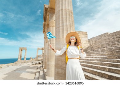 Young Traveler Woman With Greek Flag At The Ancient Greek Ruins. Tourism In Greece Concept