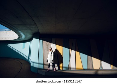 Young traveler woman in white winter coat standing against colorful wall with geometric pattern under the bridge in Norway. Urban background. Art concept. - Powered by Shutterstock