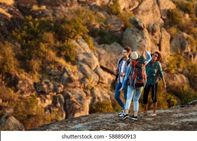 Young Travelers With Backpacks Smiling, Giving Highfive, Walking In Canyon.