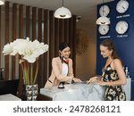 Young travelers talking and check-in register information with woman receptionist worker standing in counter hotel reception counter desk at lobby modern hotel.