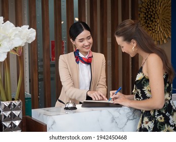 Young Travelers Talking And Check-in Register Information With Woman Receptionist Worker Standing In Counter Hotel Reception Counter Desk At Lobby Modern Hotel.