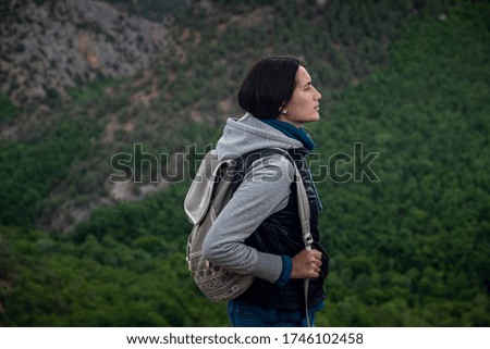 Young traveling woman with a backpack and sitting on top of the mountain cliff with relaxing mood and watching beautiful view of woods and blue sky and clouds on vacation. Asian woman travel alone.