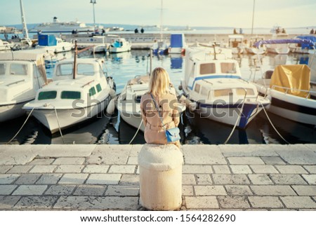 Young traveling woman in coat  sitting on sea promenade embankment enjoying the view.