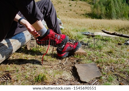 Young traveller girl taking hiking shoes off on camping during hiking in mountains. Hiker shoes off trekking boots while sitting on wooden log. Carpathian mountains, Ukraine.