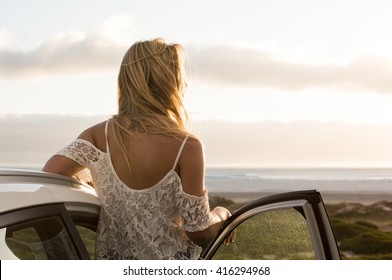 Young traveller woman enjoying sunset standing outside car. Serene woman leaning on car during sunset. Young woman on summer travel to the coast.
 - Powered by Shutterstock