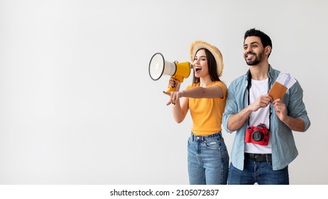 Young travellers couple with megaphone announcing excited deals for tourists, woman holding loudspeaker and pointing at free space, man holding passports and tickets, light background, panorama