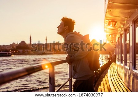 A young travelling man on a ferry floats to the shores of Istanbul, Turkey in the rays of sunset. The beginning of a great adventure.