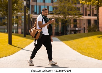 Young trendy black guy walking in the urban city area and texting on smartphone outdoors. Happy man walking and using cellphone outside - Powered by Shutterstock