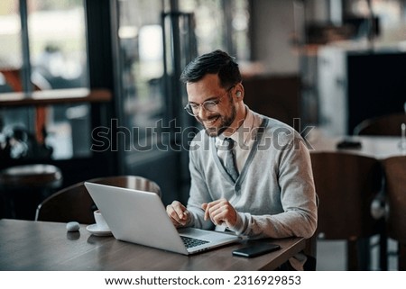A young trendy businessman is using his laptop in a coffee shop.