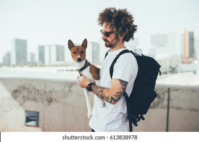 Young Trendy Hipster With Tattoos Crazy Curly Hair With His Best Friend A Little Pet Dog Basenji Breed Stands In The Urban Environment Overlooking The City Skyline After Workout