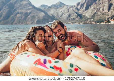 Young trendy people having fun swimming in summer vacation, relaxing on inflatable ring.