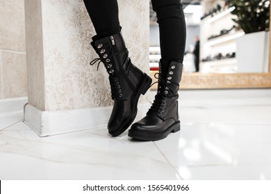 Young trendy woman in black stylish jeans in fashionable leather lace-up boots stands on the white tile in the mall. Fashion collection of women's autumn shoes. Close-up of female legs in footwear.