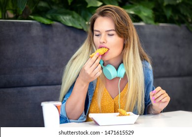 Young Trendy Woman Eating Crispy Kentucky Fried Chicken – Happy Fashionable Hipster Girl Wearing Casual Clothing And Headsets Holding Strips And Tasting Unhealthy Food At Restaurant Eatery