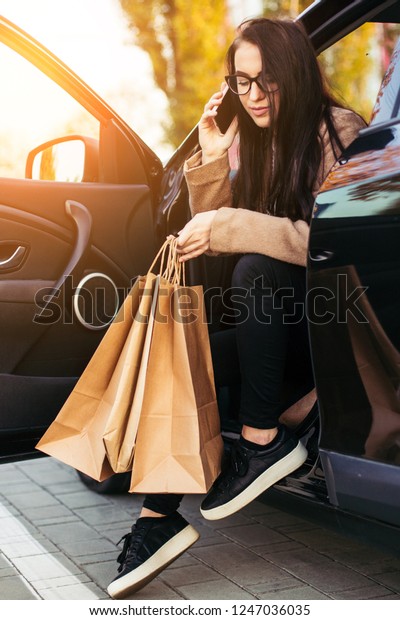 Young trendy woman with shopping bag in black\
vehicle on parking