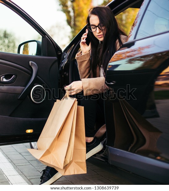 Young trendy woman with shopping bag in black
vehicle on parking