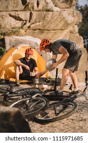 Young Trial Bikers Cooking Food On Camping Outdoors