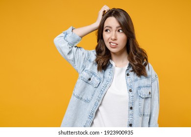 Young troubled confused sad puzzled thoughtful overthinking indignant woman 20s in stylish denim shirt white t-shirt look aside hold sctratch head isolated on yellow color background studio portrait.
