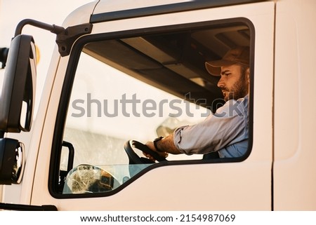 Young truck driver looking at side view mirror while driving in reverse.