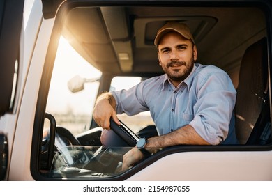 Young truck driver sitting behind steering wheel in a cabin and looking at camera.
