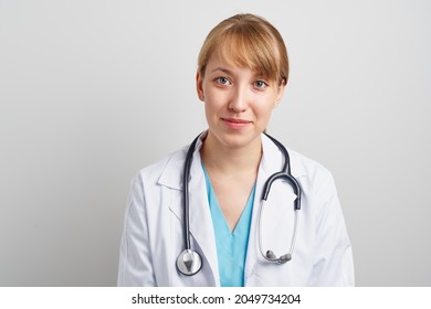 Young Trustworthy Woman Healthcare Worker With Stethoscope And In White Coat Looking At Camera And Smiling. Portrait Of Confident Family Physician Therapist On Gray Background.