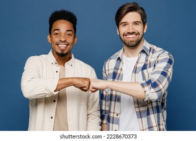 Young two friends cheerful cool smiling men 20s wear white casual shirts looking camera together give fistbump isolated plain dark royal navy blue background studio portrait. People lifestyle concept