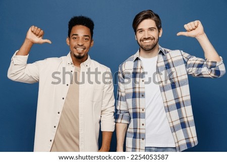 Young two friends cool happy men 20s wear white casual shirts looking camera together point thumb finger on themselves showoff isolated plain dark royal navy blue background. People lifestyle concept