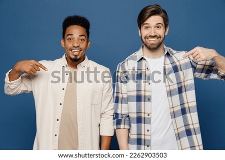 Young two friends cool happy men 20s wear white casual shirts looking camera together point index finger on themselves showoff isolated plain dark royal navy blue background. People lifestyle concept