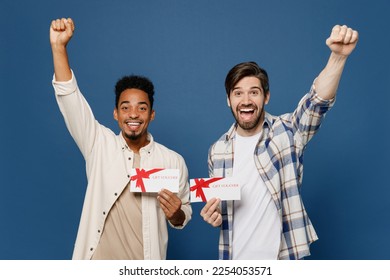 Young two friends excited surprised shocked happy men wear casual shirts together hold gift certificate coupon voucher card for store do winner gesture isolated plain dark royal navy blue background - Shutterstock ID 2254053571