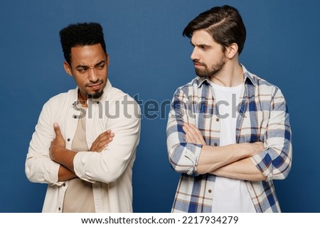Young two friends resentful sad men 20s wearing white casual shirts looking to each other together hold hands crossed folded isolated plain dark royal navy blue background. People lifestyle concept