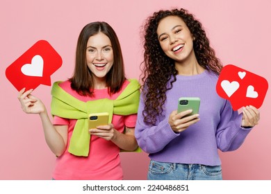 Young two friends women wearing green purple shirts together use mobile cell phone red heart form like icon sign from social network media feedback isolated on pastel plain light pink color background - Powered by Shutterstock